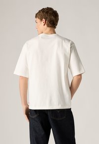 Άσπρο βαμβακερό t-shirt με άνετη εφαρμογή και κοντά μανίκια. Διαθέτει ίσια ρεγκλάν και μικρό λογότυπο στο πλάι.