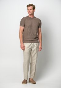 Brązowy sweter dzianinowy z krótkim rękawem w połączeniu z jasnymi lnianymi spodniami i brązowymi butami casualowymi. Prosty design o luźnym kroju i naturalnej fakturze.