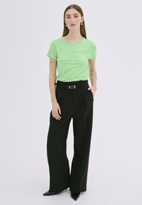 Tricou scurt, de culoare verde deschis, asortat cu pantaloni negri cu talie înaltă și croi larg, având un brâu elegant și pantofi negri cu vârful ascuțit.