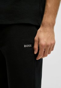 Zwarte top en broek met wafelstructuur en het 'BOSS' logo in zilveren borduursel op het rechterbeen. Heeft een ontspannen pasvorm en subtiele ontwerpelementen.