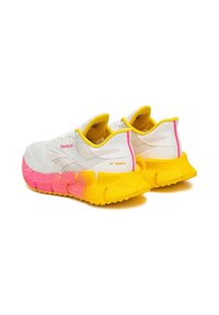 Biele bežecké tenisky Reebok s jasne ružovo-žltými gradientovými podrážkami a žltým lemovaním, zobrazené zozadu a z bočného uhla.