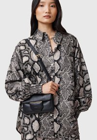 Blusa con stampa serpente nera e crema dal taglio fluido; abbinata a una piccola borsa a tracolla in pelle nera con chiusura dorata.