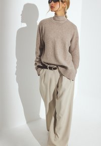 Helle beige Strickpullover mit einem gerippten Ausschnitt, kombiniert mit lockeren, cremefarbenen Hosen mit Plissee-Details und einem dunklen Gürtel.