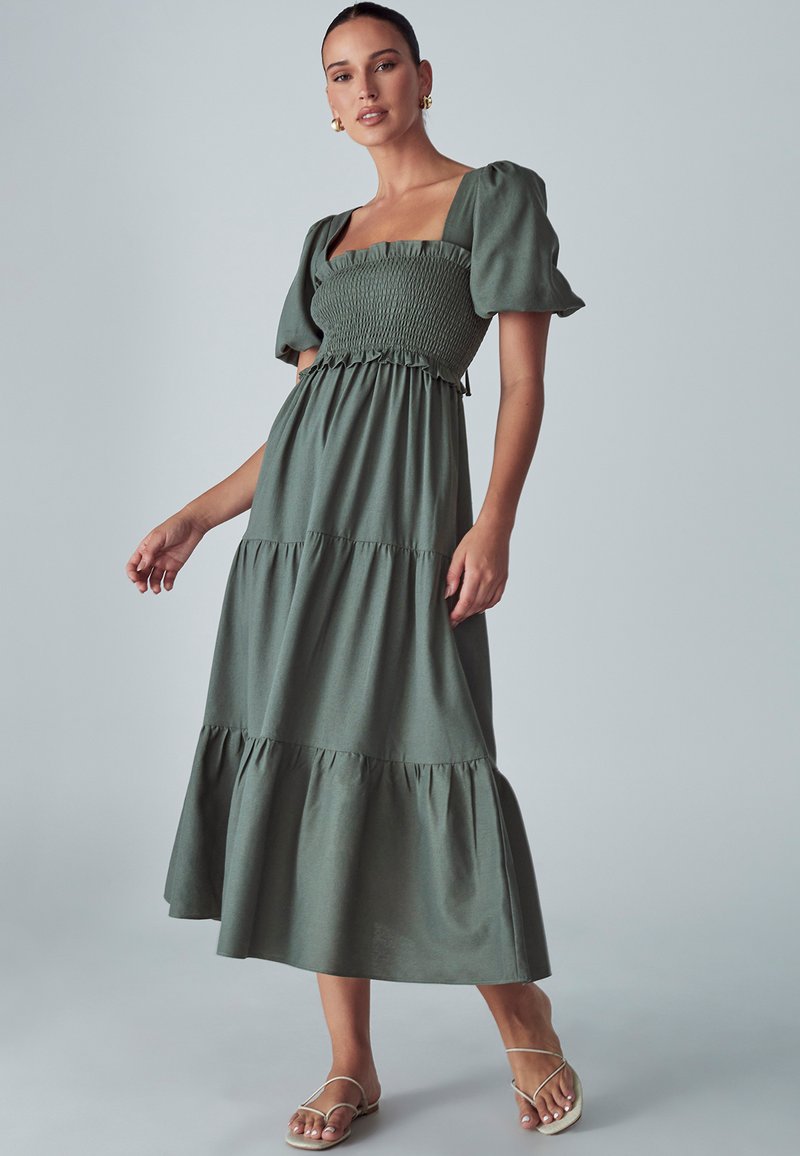 Zelena maxi haljina sa četvrtastim izrezom, naboranim rukavima, naboranim tijelom i višeslojnim rubom. Napravljena od lagane tkanine s mekim teksturom.