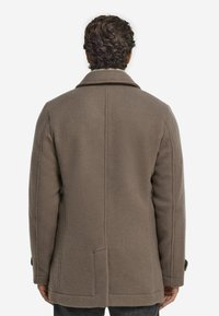 Brun ullkappa med en strukturerad silhuett, som har en bred krage, sidofickor och en mjuk textur. Bakvy, medellång design.