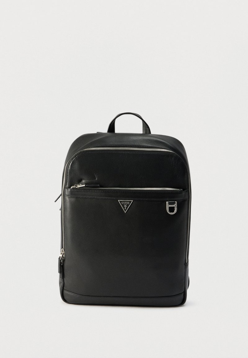 Sac à dos en cuir noir avec fermetures éclair argentées, poche avant zippée, logo Guess en métal et poignée supérieure sur fond blanc uni.