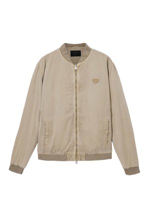 Chaqueta bomber beige con cremallera frontal, puños y dobladillo acanalados, con un logo de corazón bordado en el pecho izquierdo. Textura de tela lisa.