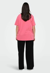 Różowa bawełniana koszulka o luźnym kroju, z okrągłym dekoltem i krótkimi rękawami, zestawiona z czarnymi spodniami szerokimi w nogawkach oraz białymi sneakersami.
