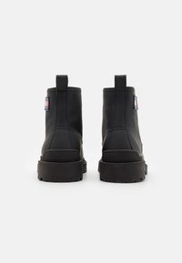 Svarta läderankelstövlar med texturerad yta, rund tå och stabil gummisula. Har en dragflik och en logotyp-patch på sidan.