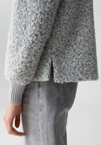 Helles graues, strukturiertes Sweatshirt aus Schlaufenstoff; mit gerippten Bündchen und einem gespaltenen Saum, kombiniert mit grauer Jeans.