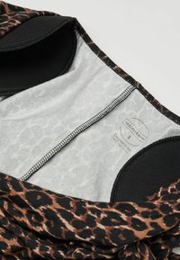 Tela de estampado de leopardo con tonos de marrón y negro. Textura suave, interior forrado, borde negro y una etiqueta de cuidado en el interior.