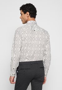 Wit shirt met patroon van veelkleurige diamanten, voorzien van een hoge kraag en manchetten met knopen, gecombineerd met een donkere broek.