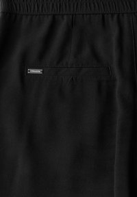 Shorts noirs en tissu lisse avec une taille élastique et une poche arrière, dotée d'une petite étiquette de marque et d'un détail de couture subtil.