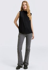 Top nero senza maniche con collo alto, abbinato a jeans grigi a zampa e scarpe nere robuste. Texture liscia e design semplice.