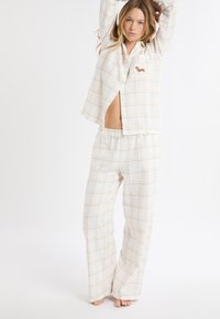Biały zestaw piżam w kratę z jasnobrązowymi liniami, koszula zapinana na guziki z długimi rękawami i haftem jamnika oraz spodnie z elastycznym pasem.