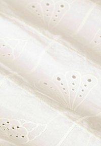 White linen fabric featuring intricate floral embroidery with cut-out details. Textured surface with a smooth finish and subtle sheen.