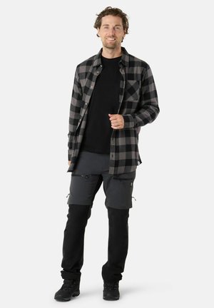 Heren flanellen overhemd in zwart en grijs geruite patroon, gecombineerd met donkergrijze ritskorte broek tot de knie en zwarte laarzen.