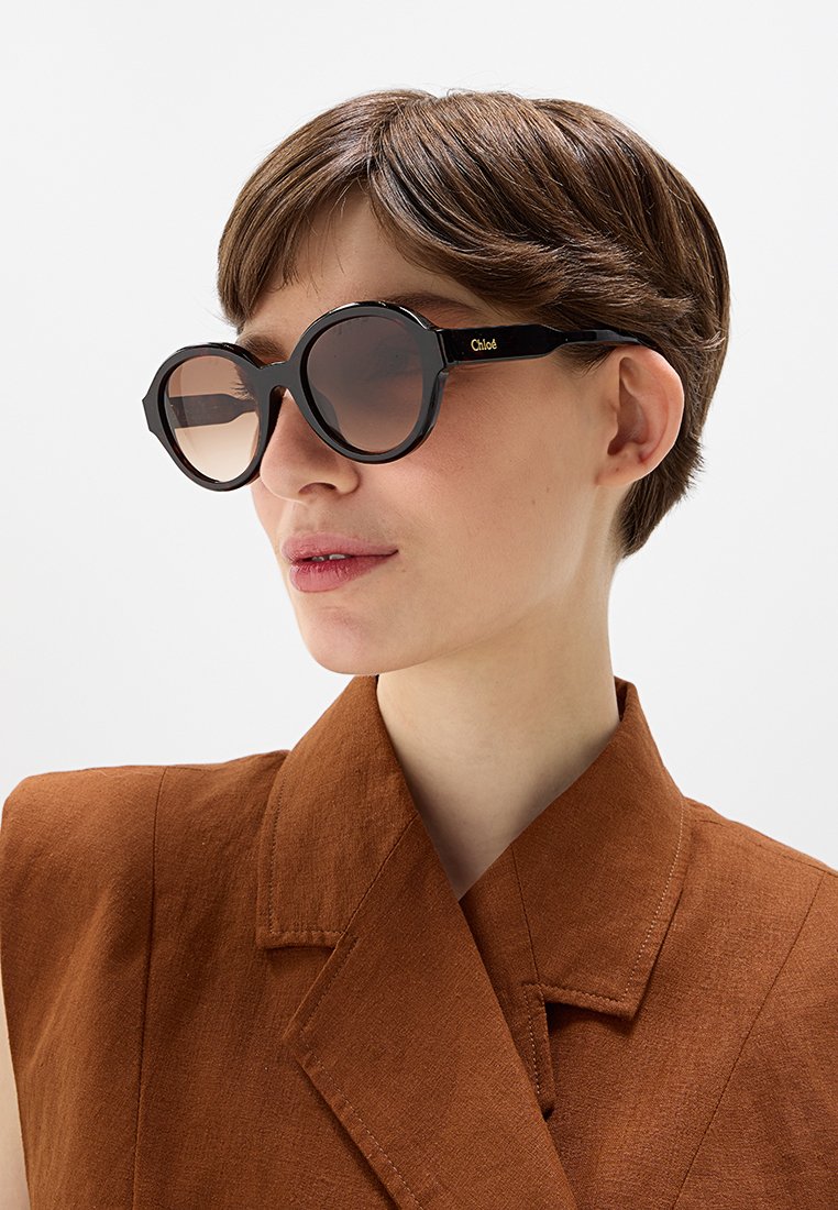 Zwarte oversized zonnebril met een geometrisch ontwerp, gradient lenzen en een gouden "Chloé" branding aan de zijkant.
