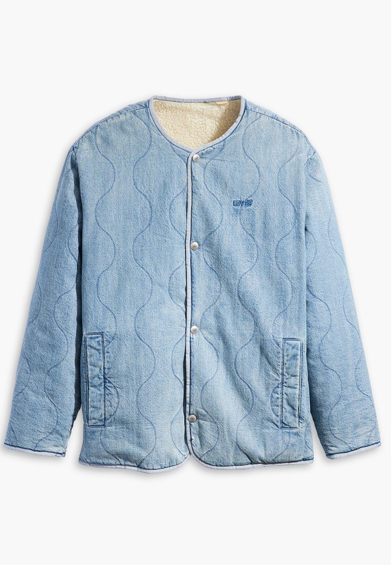 Chaqueta acolchada de color azul claro con cuello redondo, botones a presión, dos bolsillos laterales y un forro suave de color crema. Presenta un patrón ondulado.
