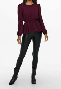 Burgundyröd peplumtop med puffärmar, kombinerad med svarta leggings i konstläder och ankelstövlar. Slät textur och figurnära design.