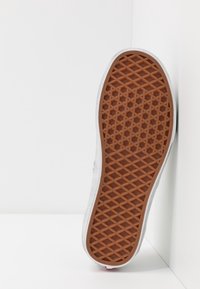 Semelle de sneaker en caoutchouc avec un motif brun texturé et un bord blanc. La semelle présente un design en nid d'abeille pour une meilleure adhérence et durabilité.