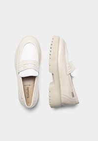 Beige synthetische Slippers mit einem weißen Lederakzent, ausgestattet mit einer dicken, strukturierten Sohle und einem dekorativen Riemen über dem Spann.