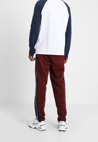 Pánský set obsahující bílé a námořnické dlouhé rukávy a vínové tepláky se bočními pruhy. Bílé tenisky dokončují outfit.