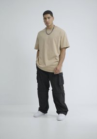 Beige oversized t-shirt met korte mouwen, gecombineerd met zwarte cargobroek met zijzakken. Schoeisel is witte sneakers.