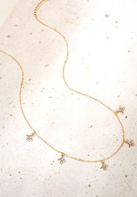 Złoty naszyjnik łańcuszkowy z pięcioma akcentami w kształcie kwiatów, z każdą ozdobioną małym, przezroczystym kamieniem szlachetnym. Delikatny design o finezyjnej fakturze i blasku.