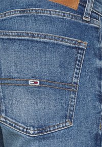 Jeans i denim med en medelblå tvätt, synliga sömmar och en lapp av tan läder ovanför bakfickan med en liten logotypdetalj.