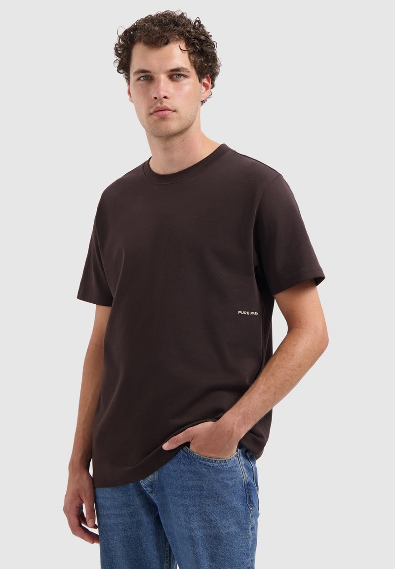 Bruine korte mouwen t-shirt gemaakt van katoen met een relaxte fit. Heeft een klein wit tekstlogo aan de linkerzijde, nabij de taille.