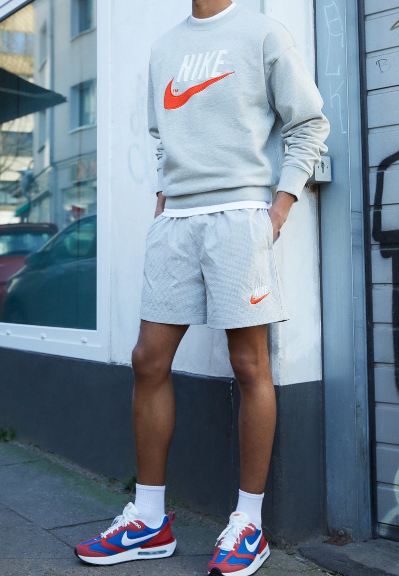 Gray sweatshirt with orange Nike logo, paired with light gray shorts featuring textured design and a matching Nike logo. Red and blue sneakers.