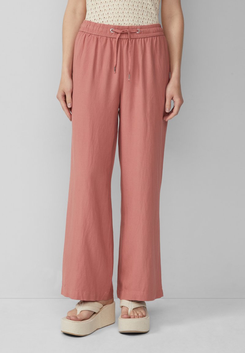 Lichtroze, wijde broek gemaakt van zachte stof met een elastische tailleband en een trekkoord. Gecombineerd met crèmekleurige plateau-sandalen.