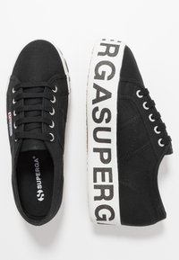 Black canvas sneakers with a textured upper, white rubber sole, and bold "SUPERGA" branding on the side. Featuring round laces and metal eyelets.