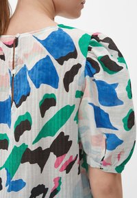 Kurzes Kleid mit kurzen Ärmeln, das einen bunten abstrakten Druck in Blau, Grün, Schwarz und Pink zeigt, mit einem strukturierten Stoff und einem Knopfdetail im Rücken.