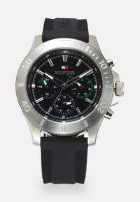 Chronograph-Uhr mit schwarzem Zifferblatt, silbernem Edelstahlgehäuse und schwarzem Gummiband; verfügt über grüne Akzente und mehrere Subzifferblätter.