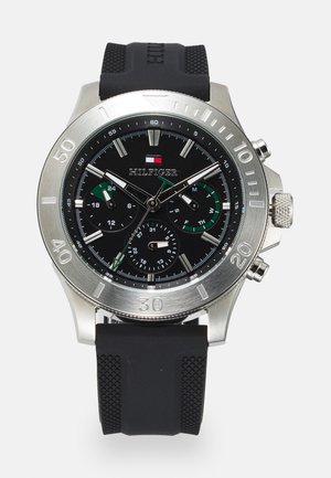 Montre chronographe avec un cadran noir, un boîtier en acier inoxydable argenté et un bracelet en caoutchouc noir ; présente des accents verts et plusieurs sous-cadrans.