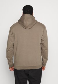 Sudadera con capucha en una tela suave de color marrón. Presenta un corte relajado, mangas y dobladillo acanalados. Costuras planas y cordón ajustable en la capucha.