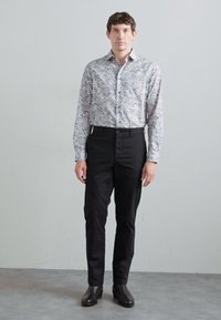 Fehér, hosszú ujjú ing virágmintával, fekete nadrággal és fekete csizmával párosítva. Az ing gombos gallérral rendelkezik és slim fit szabású.
