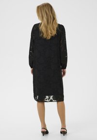 Rochie neagră din dantelă florală, cu mâneci lungi, până la genunchi. Overlay transparent cu o rochie subțire asortată, având un guler rotund și o croială lejeră.