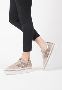 Sneakers beige chiaro con accenti metallici dorati, tomaia in tessuto texturizzato e una spessa suola piatta bianca, con chiusura con lacci.