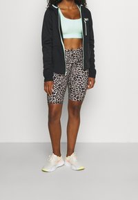 Svart zip-up hoodie med mintgröna detaljer, ljusblå sportbh och beige leopardmönstrade cykelshorts. Vita och neongröna sneakers.