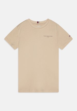 Bež T-majica iz bombaža s krojem pri vratu, kratkimi rokavi in majhnim logotipom na prsih. Ima šivano podrobnost na rami.