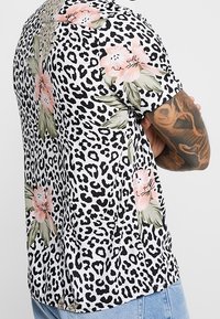Kortärmad skjorta med svartvitt leopardmönster och rosa blommönster, tillverkad av lätt tyg. Visar en avslappnad passform.