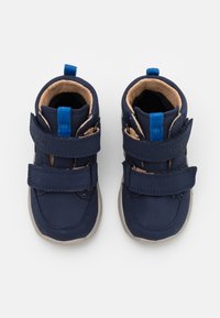 Marineblaue Kleinkinderschuhe mit zwei verstellbaren Klettverschlüssen, beigem Innenfutter, Gummisohlen und einer kleinen blauen Fersenlasche.