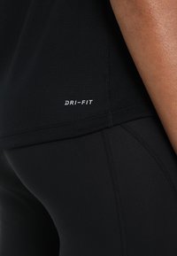 Camiseta de rendimiento Dri-FIT negra con una textura de malla transpirable, que presenta un logo en blanco en el dobladillo. Diseño liso y ajustado.