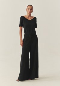 Čierny top s krátkym rukávom a výstrihom do V, skombinovaný s čiernymi širokými nohavicami s vysokým pásom. Hladká tkanina s lesklým povrchom, minimalistický dizajn.