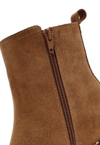 Stivale alla caviglia in suede marrone con zip laterale e linguetta di sorreggio, con una finitura liscia e una forma arrotondata.