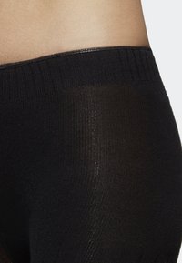 Detailní záběr pasu a boků osoby oblečené v černých žebrovaných, průhledných punčochách s širokým elastickým pasem.