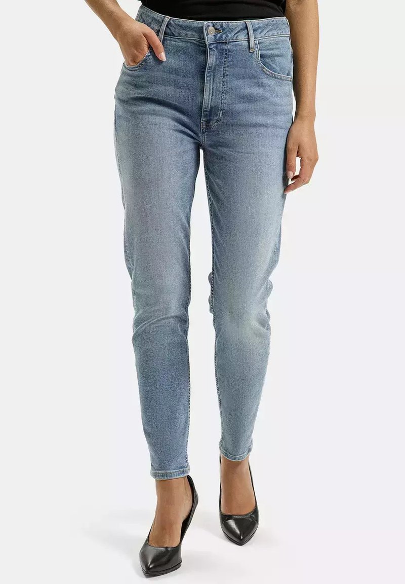 Jasnoniebieskie dżinsy z wysokim stanem o zwężanym kroju, z klasycznym pięcio-kieszeniowym wzorem i wyblakłą fakturą. Noszone z czarnymi szpilkami.